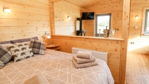 A wooden cabin room with a bed, a nightstand, a mirror, and a window. - Badgers Sett (Darlington)