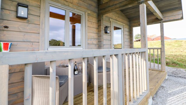 A wooden cabin with a porch, wicker furniture, and a bottle of wine on the table. - Badgers Sett (Darlington)