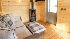 A cozy cabin interior with a sofa, ottoman, and a wood-burning stove. - Badgers Sett (Darlington)