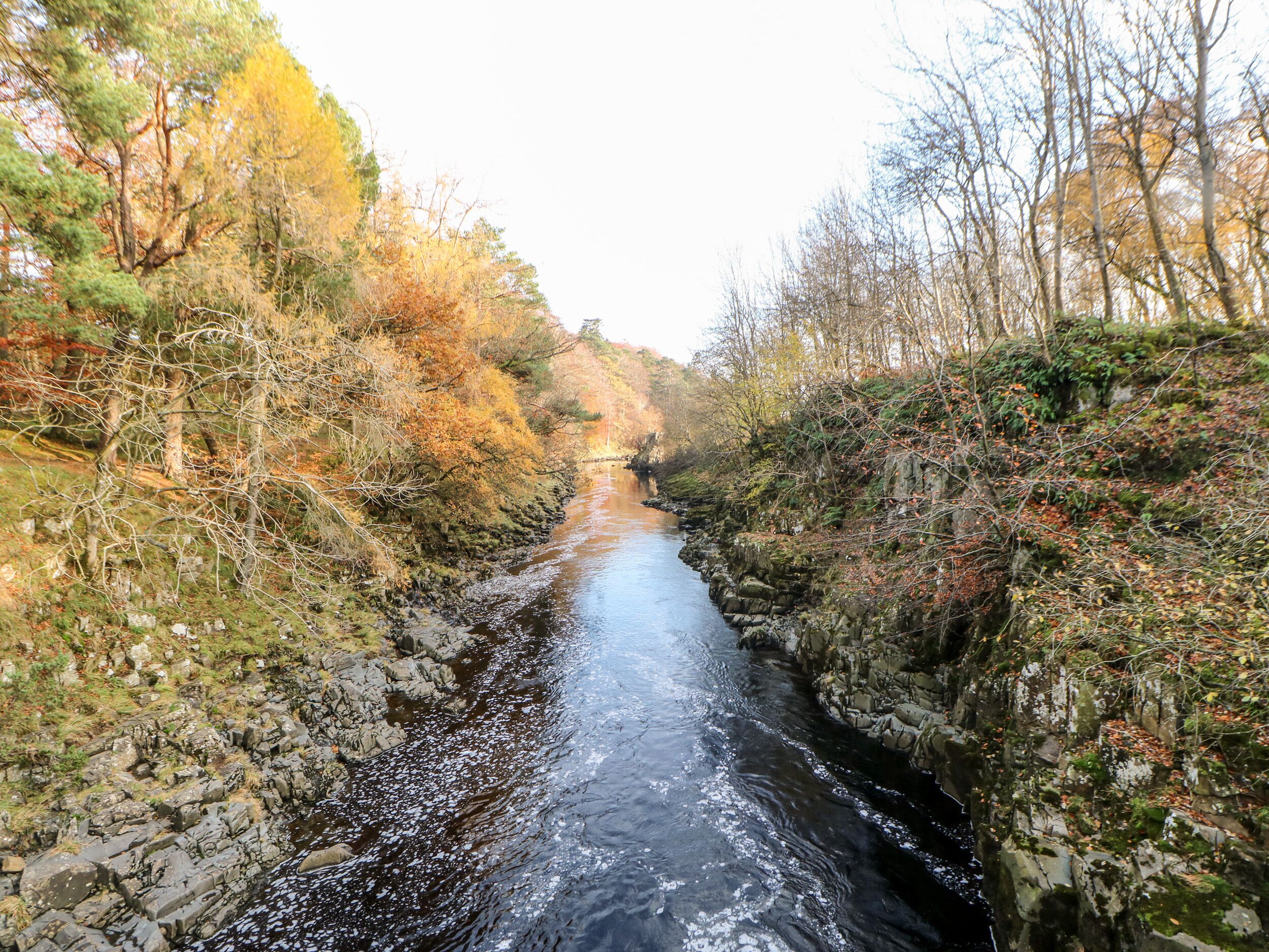 Une rivière étroite, bordée de rives rocheuses et de feuillage automnal.