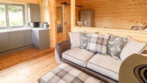 A cozy cabin interior with a kitchenette, a sofa with plaid cushions, and a wooden ceiling. - Badgers Sett (Darlington)