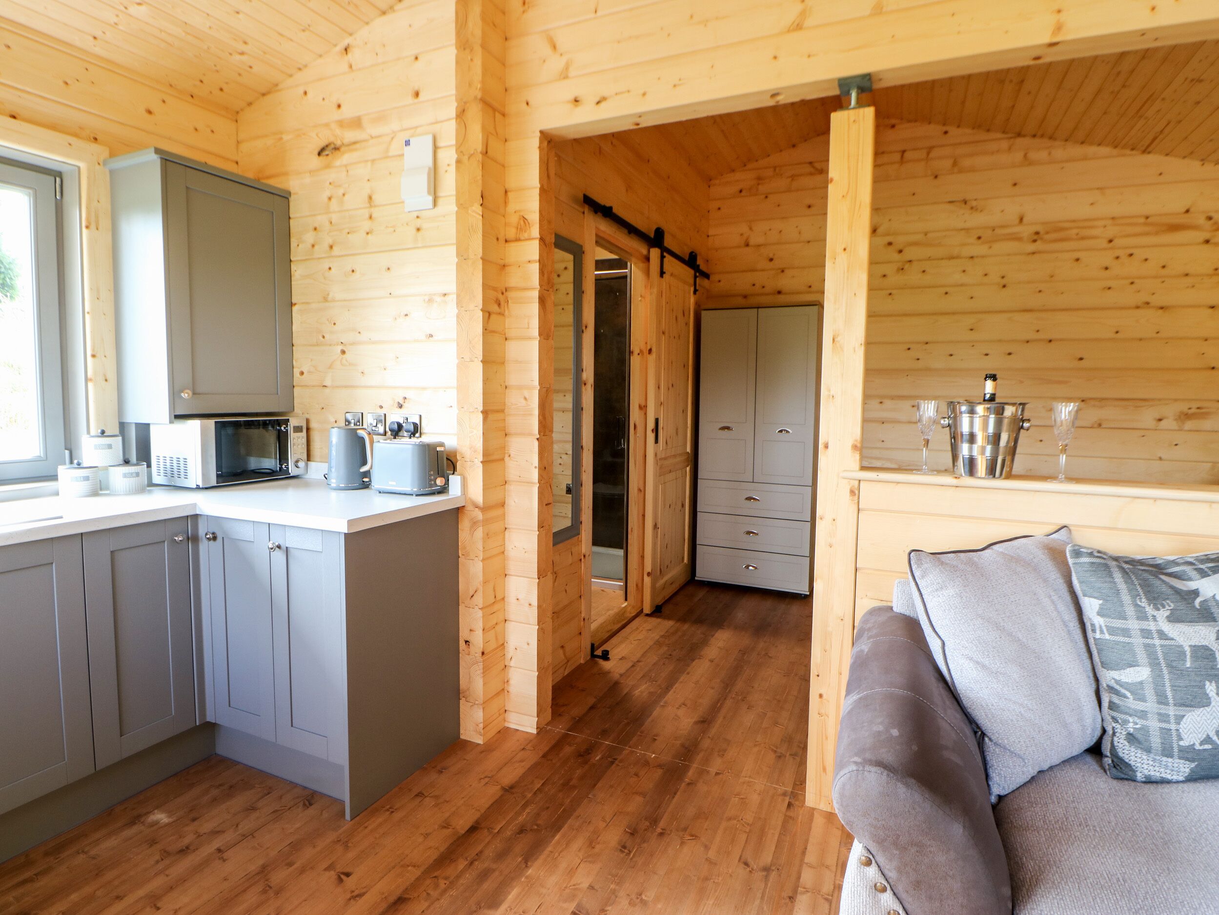 A wooden cabin interior with a kitchen area, a dining space, and a living area with a sofa.