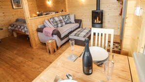 A cozy wooden cabin interior with a sofa, a table set for dining, and a wood-burning stove. - Otters Holt (Darlington)
