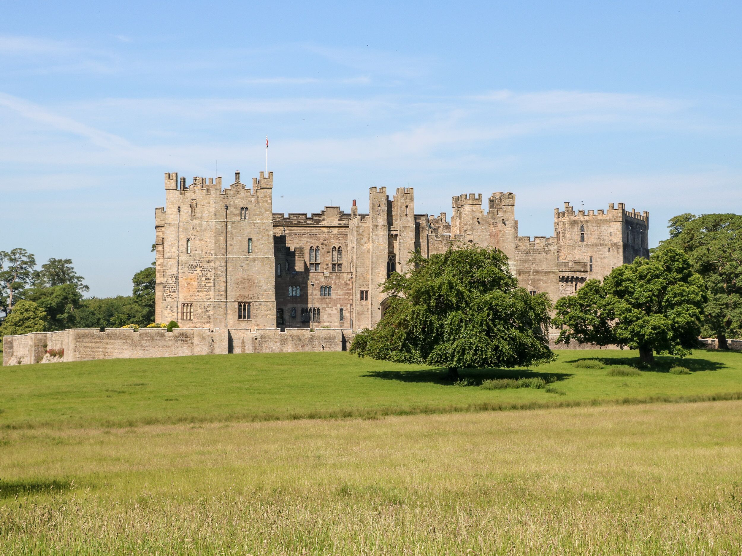 A large, historic castle with multiple towers and a well-maintained lawn in the foreground.
