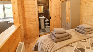 A wooden cabin-style room with a bed, a bathroom with a sink and mirror, and a wardrobe. - Otters Holt (Darlington)