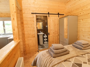 Een houten blokhut van binnen, met een bed, een badkamer met een wastafel en spiegel, en een kledingkast.