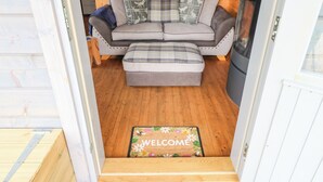 A cozy cabin interior with a sofa, ottoman, and a welcome mat at the entrance. - Otters Holt (Darlington)