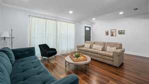 Una sala de estar moderna con un sofá verde oscuro, un sofá color beige, una mesa redonda de centro y un sillón negro.