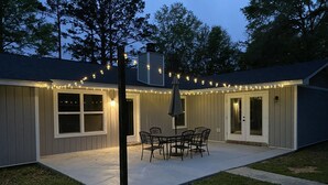 Un patio techado con mesa y sillas, luces colgantes y una zona de estar cubierta.