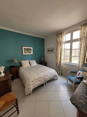 Un dormitorio con cama, dos mesitas de noche, una silla, un escritorio y una ventana con cortinas.