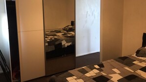 A room with a large mirror, a bed with a patterned bedspread, and a small table with a geometric-patterned table runner. - Immaculate 1-bed Apartment in Stoke-on-trent (Stoke-on-Trent)