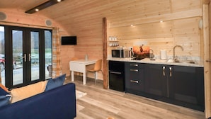 A cozy cabin interior with a dining area, kitchen, and a large window overlooking a scenic view. - The Stag - Crossgate Luxury Glamping (Penrith)