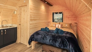 A cozy cabin room with a wooden interior, a bed with a dark blue bedspread, a window with a forest view, and a sink with a marble countertop. - The Stag - Crossgate Luxury Glamping (Penrith)