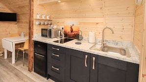 A modern kitchen with wooden walls, a marble countertop, and stainless steel appliances. - The Stag - Crossgate Luxury Glamping (Penrith)
