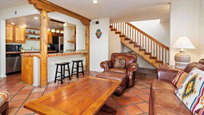 Un amplio salón con una mesa de comedor de madera, sofás de cuero, una cocina con armarios de madera y una escalera.