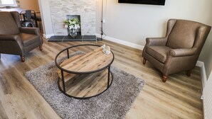 A living room with two brown leather armchairs, a round coffee table, a flat-screen TV mounted on the wall, and a stone fireplace.