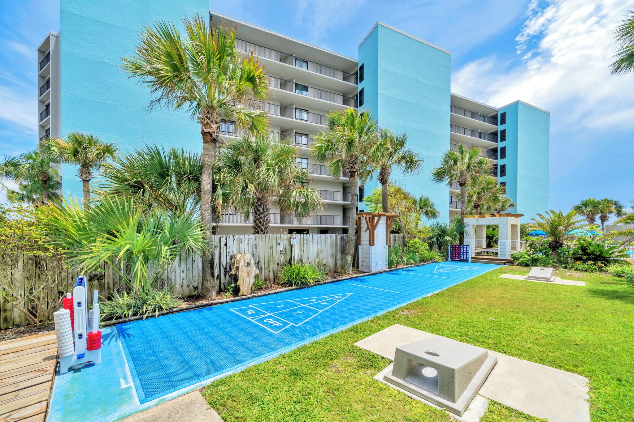 A pool area with a shuffleboard court, surrounded by palm trees and a modern building.