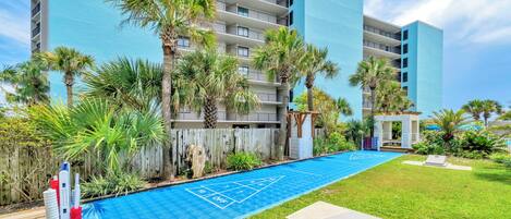 A pool area with a shuffleboard court, surrounded by palm trees and a modern building.