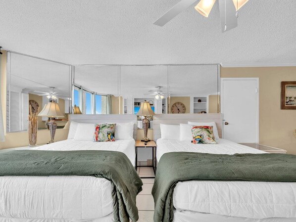 Habitación de hotel con dos camas, un espejo grande, un reloj y vista al mar.