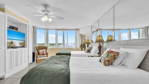 A hotel room with a large bed, a smaller bed, a television on the wall, and a ceiling fan.
