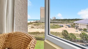 A view from a window overlooking a beach, a parking area, and a building with a flat roof.
