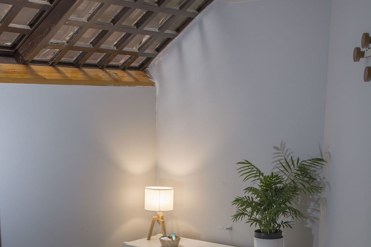 A bedroom with a bed, a bedside table with a lamp, a potted plant, a white console table, and a red box.