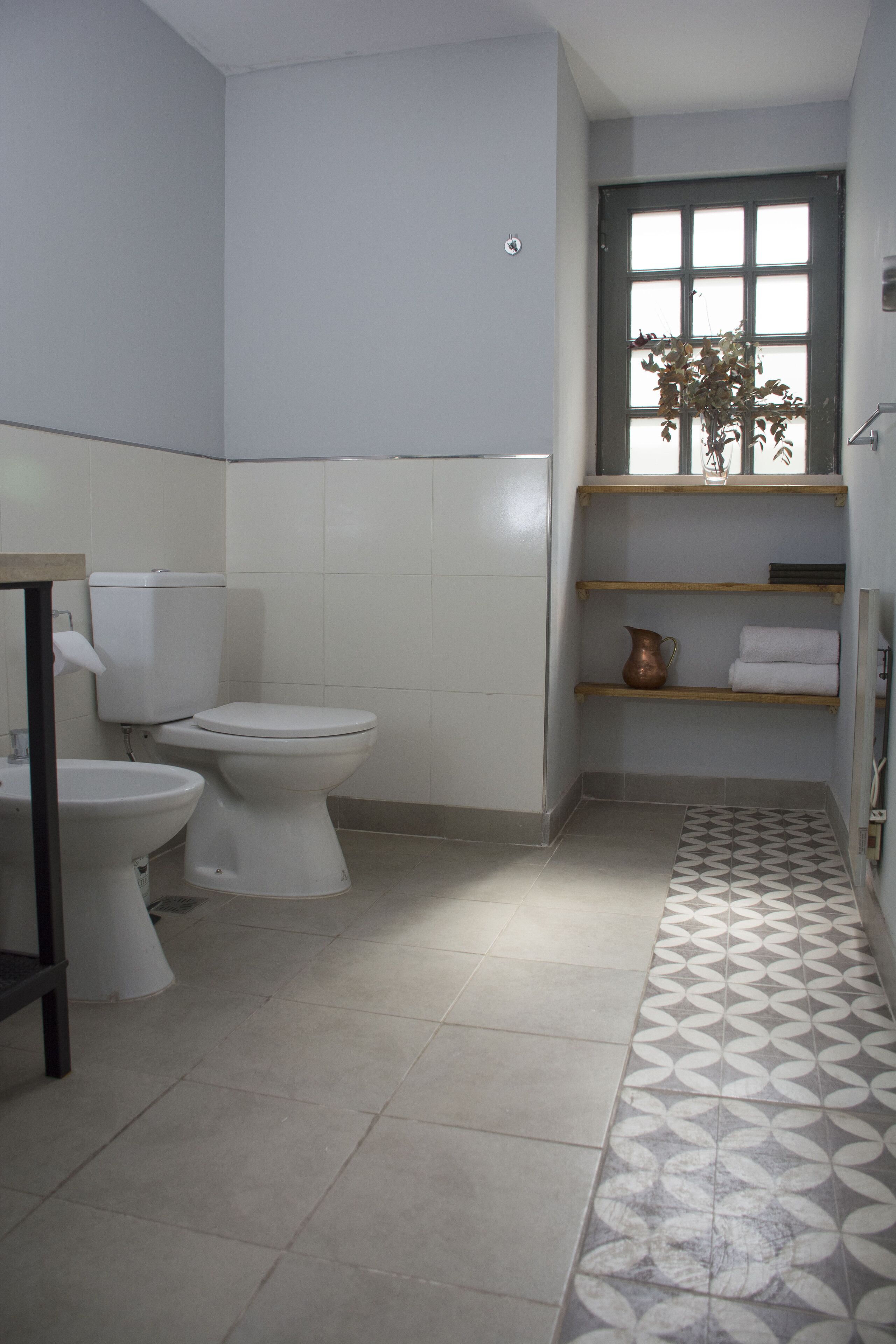 A compact bathroom with a toilet, bidet, and a shelf with towels and a vase.