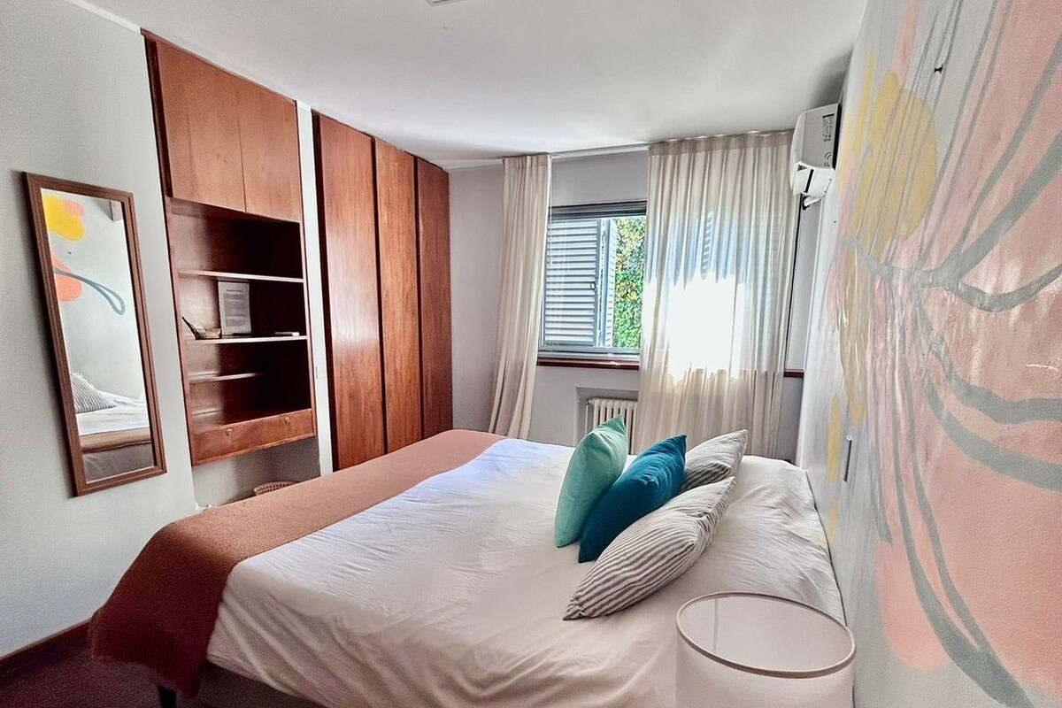 A bedroom with a bed, bedside table, wardrobe, and a window with curtains.