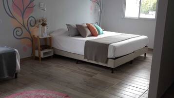 Un dormitorio con cama, mesita de noche, ventana y un mural decorativo.