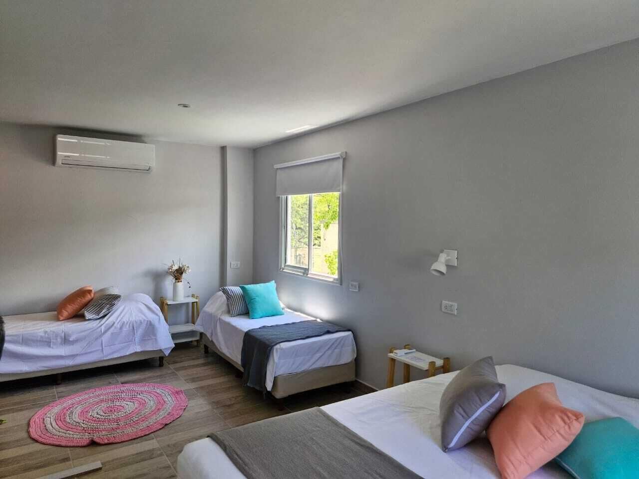 A room with two single beds, a window with a view, a small table, and a wall-mounted air conditioner.