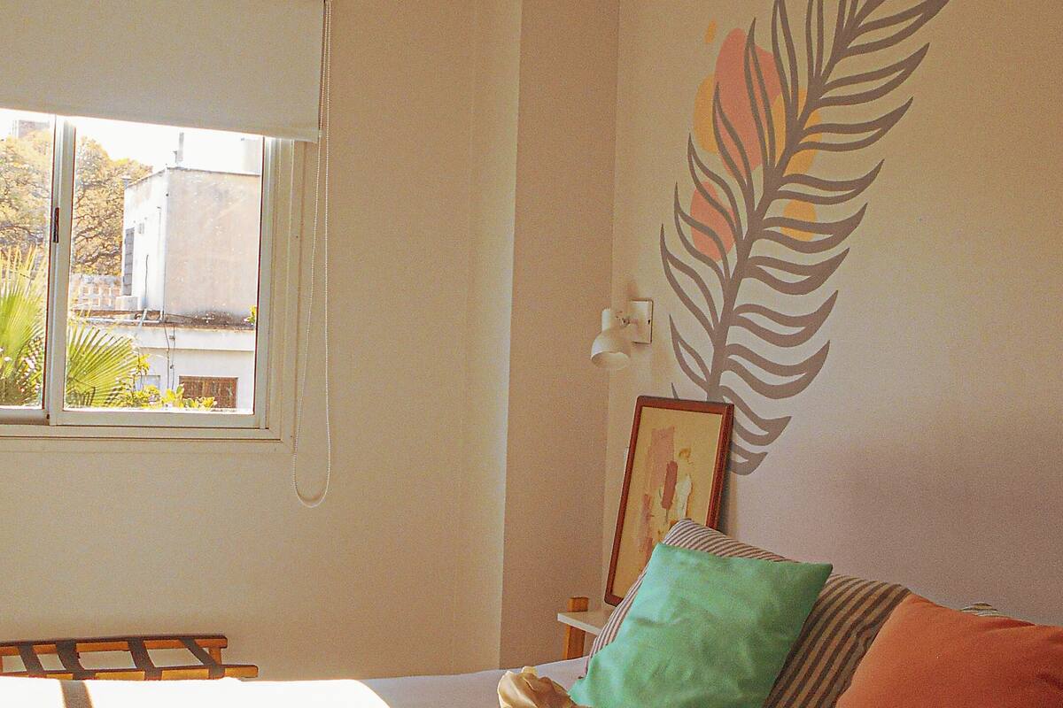 A bedroom with a bed, pillows, a window, and a wall decoration.
