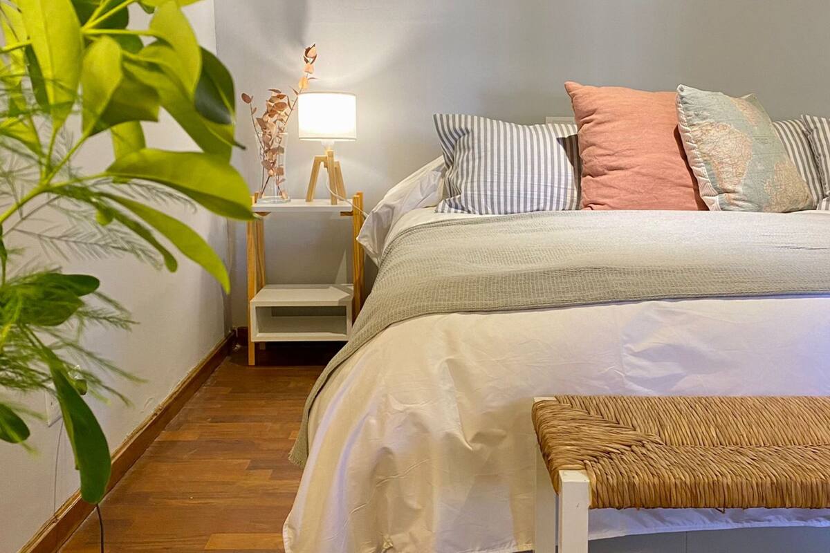 A neatly arranged bedroom with a bed, bedside table, lamp, and a bench.