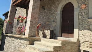 A stone building with a wooden balcony, a large arched door, and steps leading to the entrance. - IL PIANETTO (Pieve Fosciana)