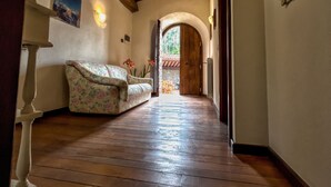 A wooden-floored hallway with a floral sofa, a wooden ceiling, and a door leading outside. - IL PIANETTO (Pieve Fosciana)