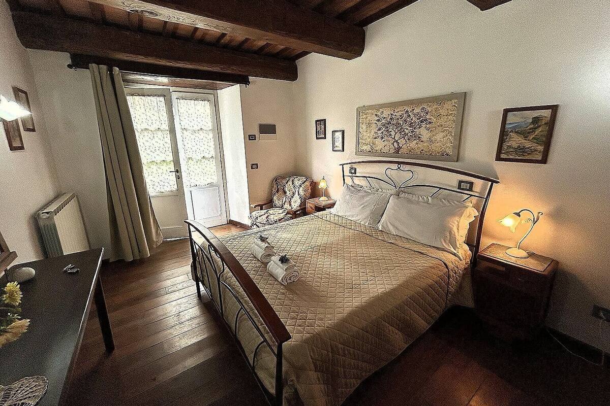 Un dormitorio con cama, escritorio, silla, lámpara y ventana con cortinas.