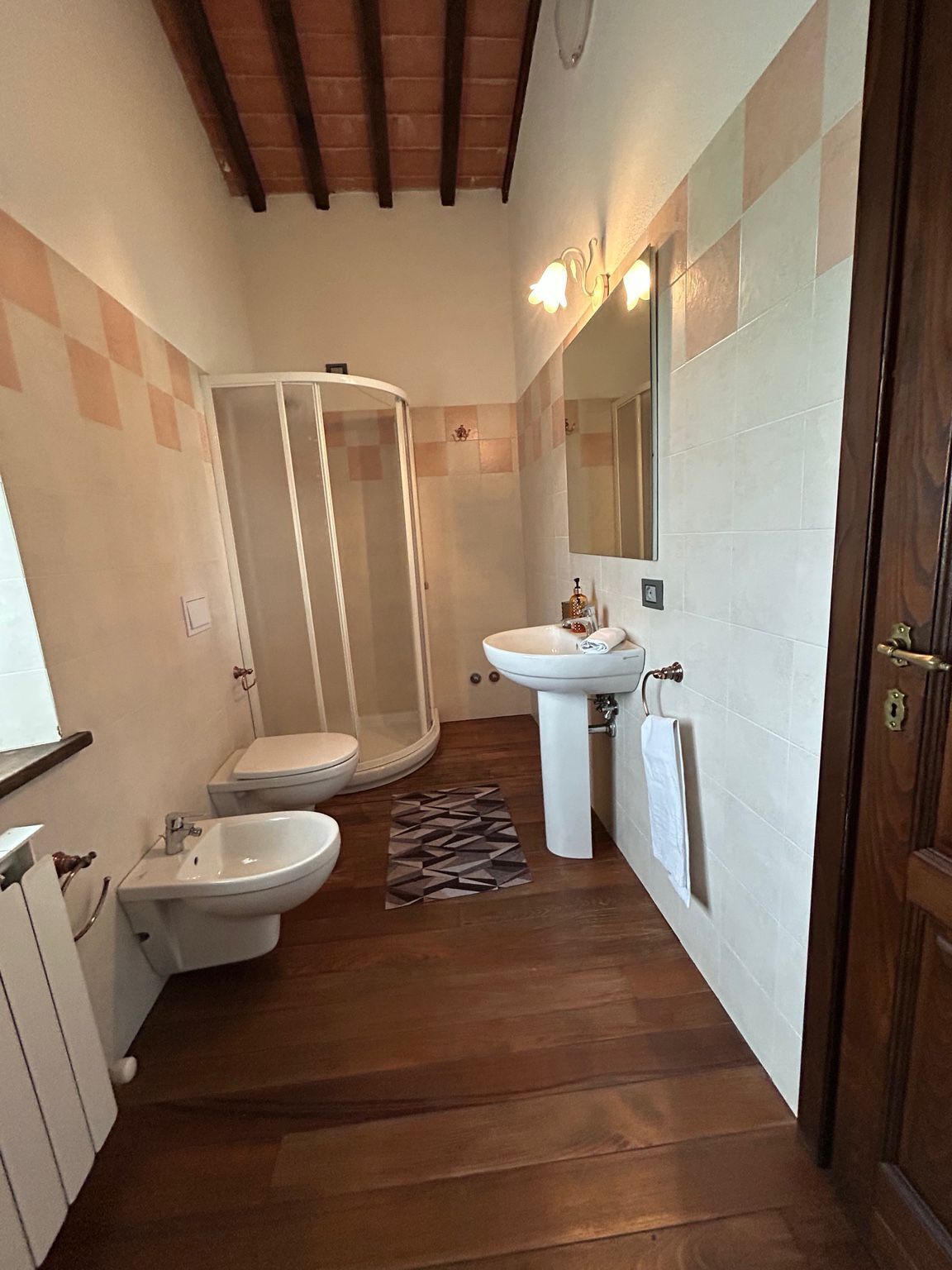 Un baño pequeño con ducha, dos lavamanos y un inodoro.