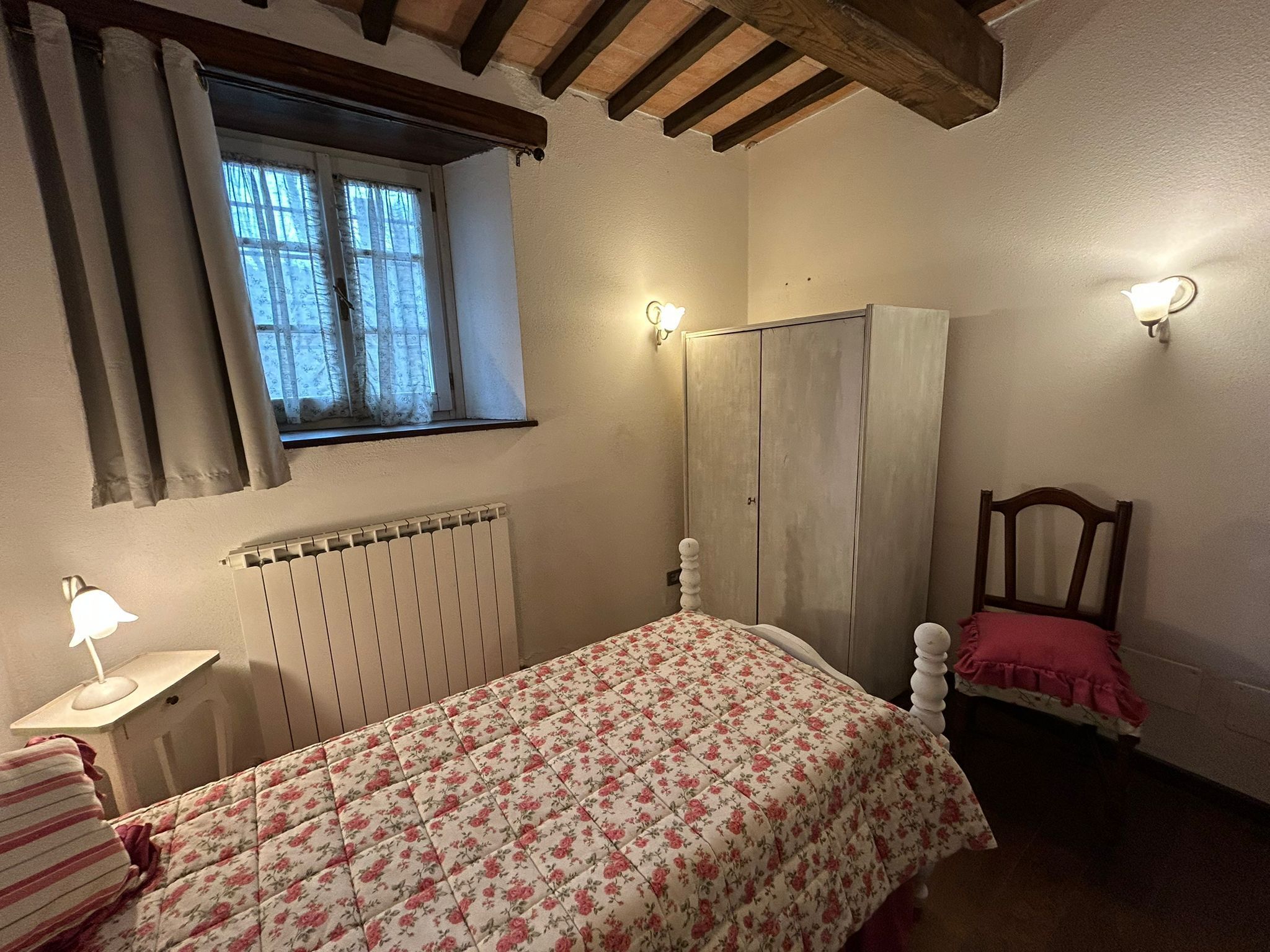 Une chambre à coucher avec un lit, un radiateur, une fenêtre avec des rideaux, une armoire et une chaise.