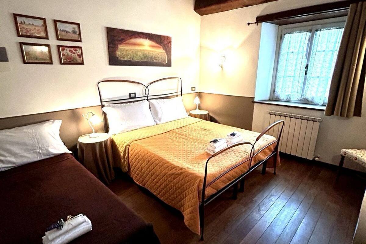 Una habitación con dos camas, una ventana con cortinas, un radiador y obras de arte colgadas en la pared.