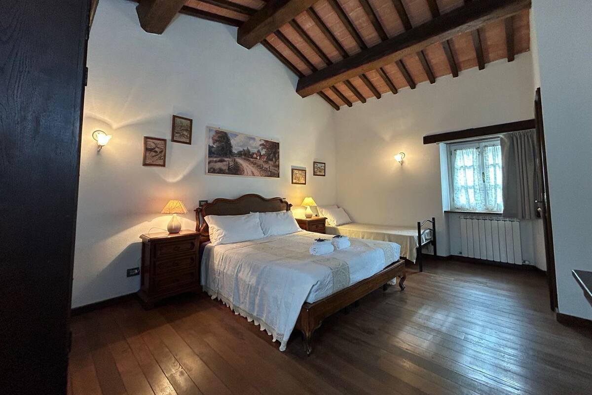 Un dormitorio con una cama de madera, dos mesitas de noche con lámparas, una ventana con cortinas y un cuadro en la pared.