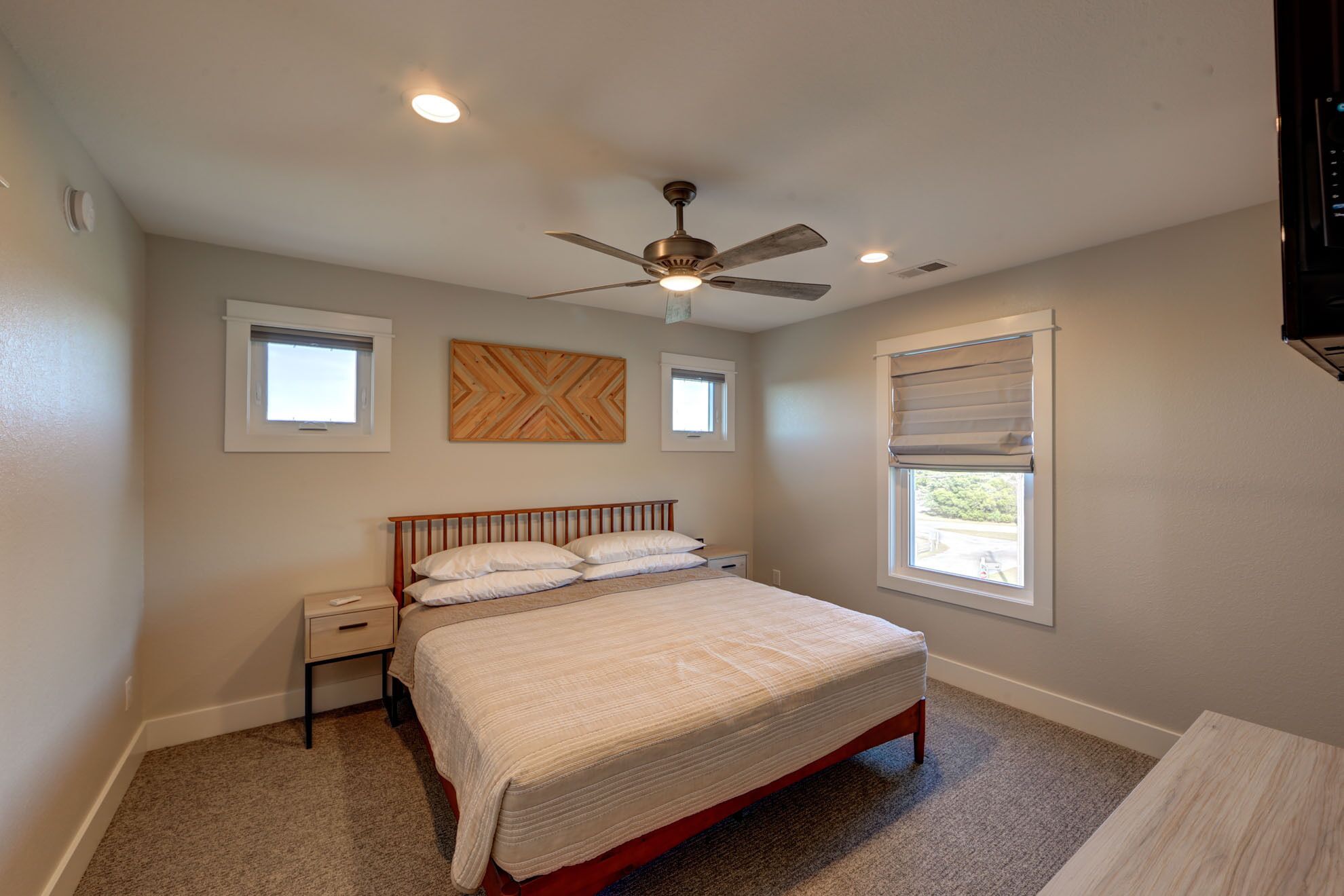 A bedroom with a bed, a nightstand, a ceiling fan, and two windows.