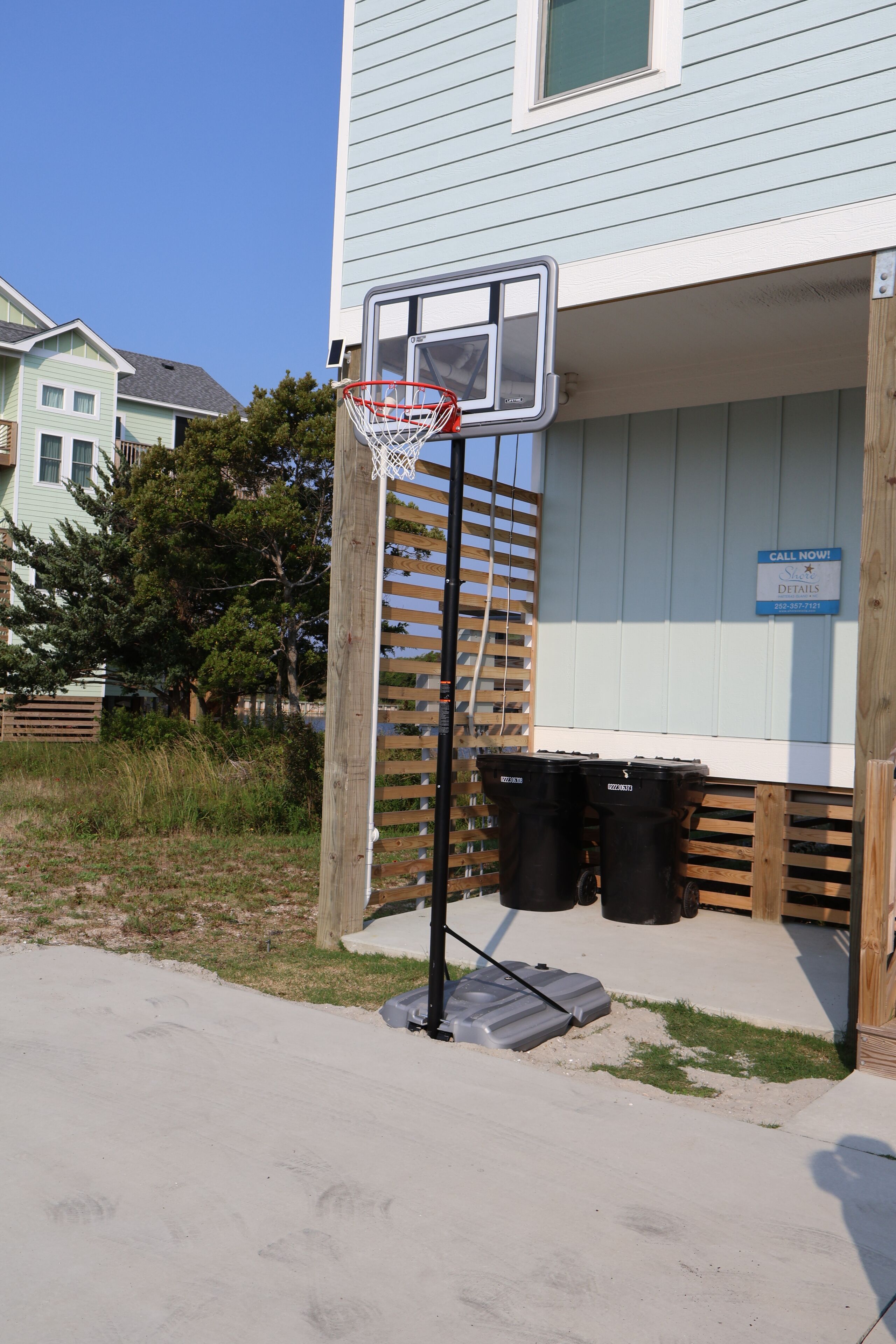 Un panier de basketball est fixé à une clôture en bois devant une maison à la façade bleue.