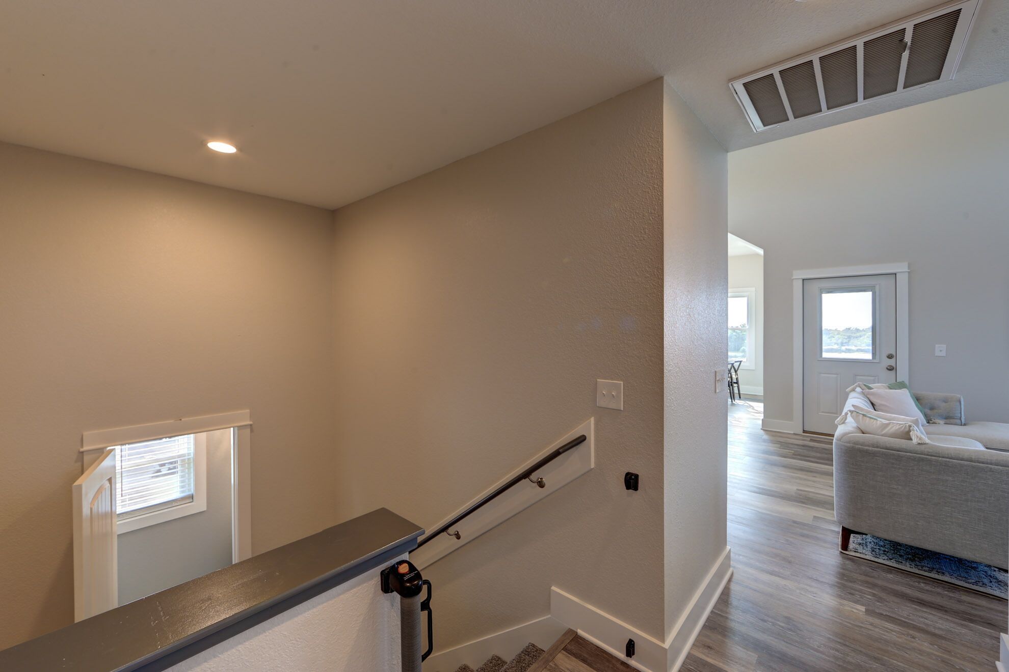 A staircase with a handrail, a window with blinds, and a door leading to a living area with a sofa.