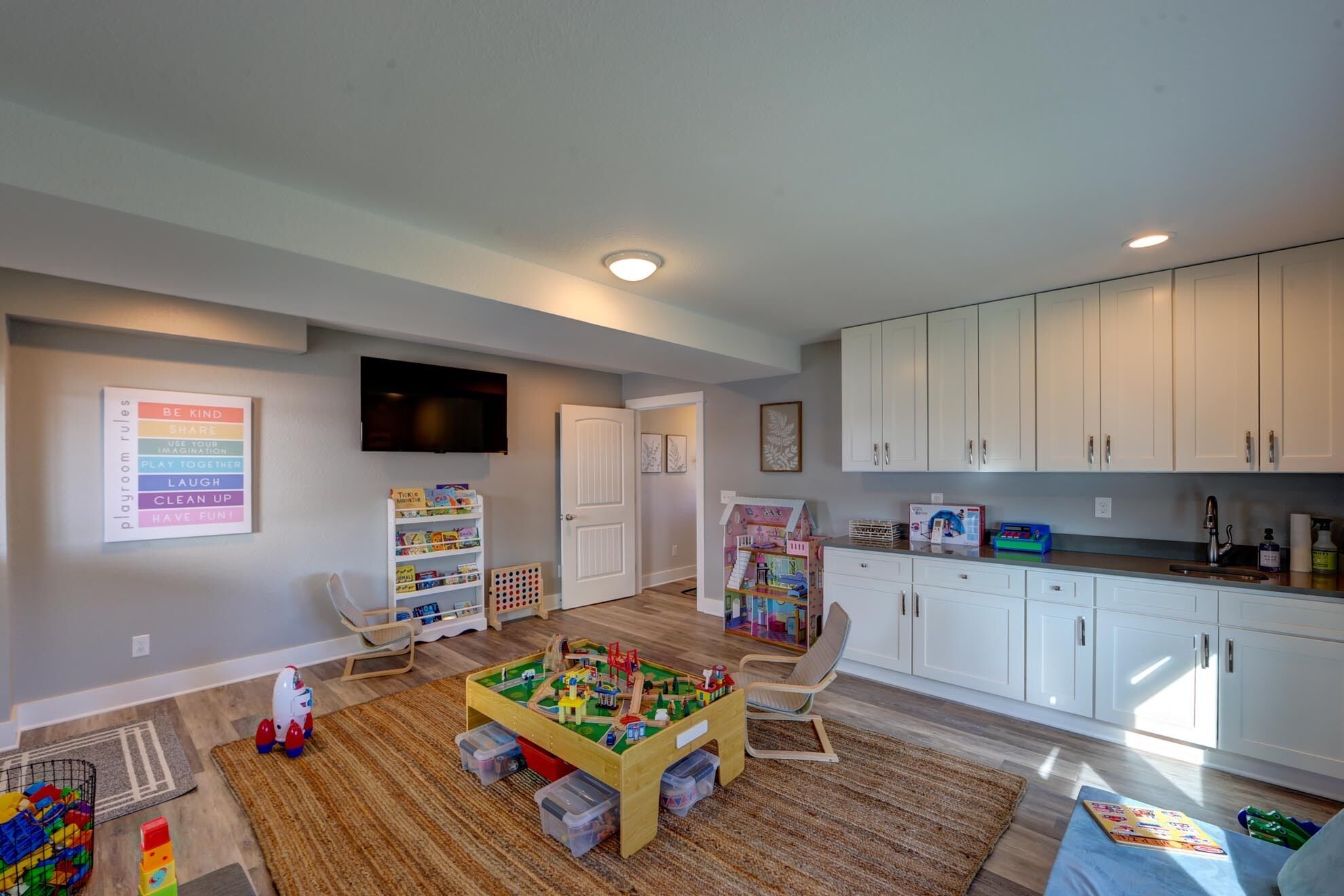 A playroom with a playroom rules poster, a television, and a play area with toys and a playhouse.