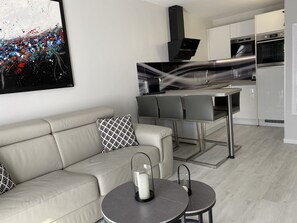 A modern kitchen with stainless steel appliances, a dining area with a table and chairs, and a living area with a sofa and a decorative pillow. - Beautiful new bright apartment facing south 100 m from the beach direct access (Cabourg)
