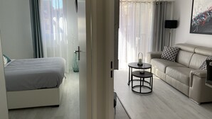 Un salon moderne avec un canapé, une petite table ronde et un lit doté d’une tête de lit blanche.