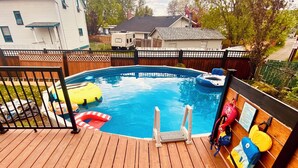 Una terraza de madera con piscina, sillas de descanso y un patio trasero cercado.