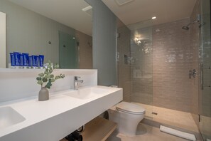 A modern bathroom with a large mirror, white sink, and a glass-enclosed shower. - The Shoals Suites and Slips (Southold)