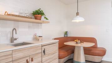 A modern kitchen with a built-in sink, wooden cabinets, a round table, and a brown leather bench.