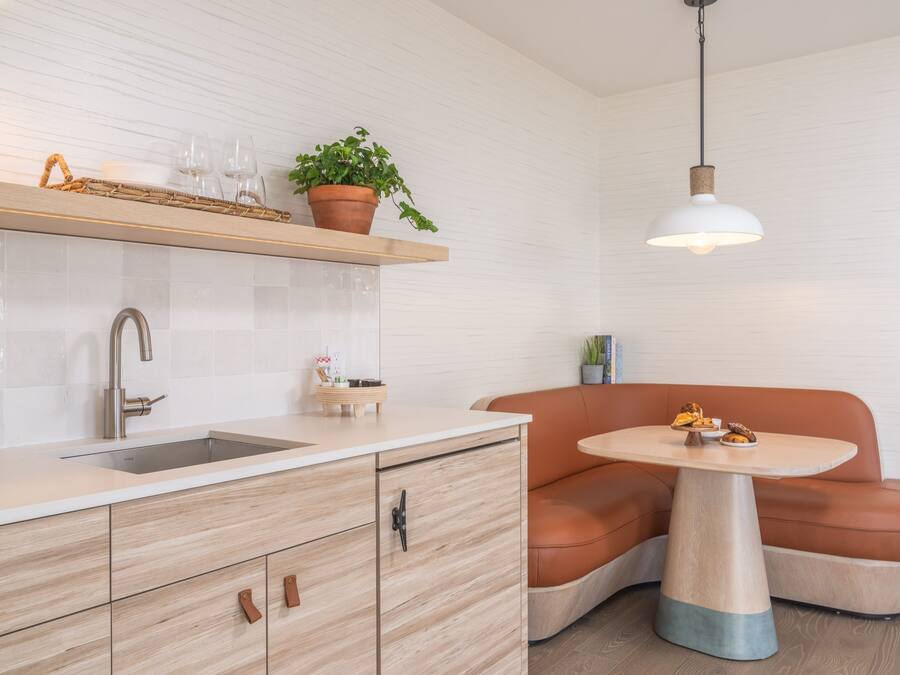 Une cuisine moderne dotée d’un évier encastré, de meubles en bois, d’une table ronde et d’un banc en cuir marron.
