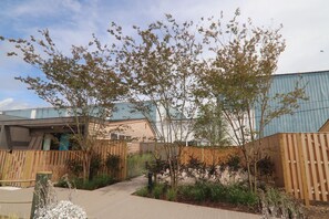 A courtyard with a wooden fence, a pathway, and a tree. - The Shoals Suites and Slips (Southold)